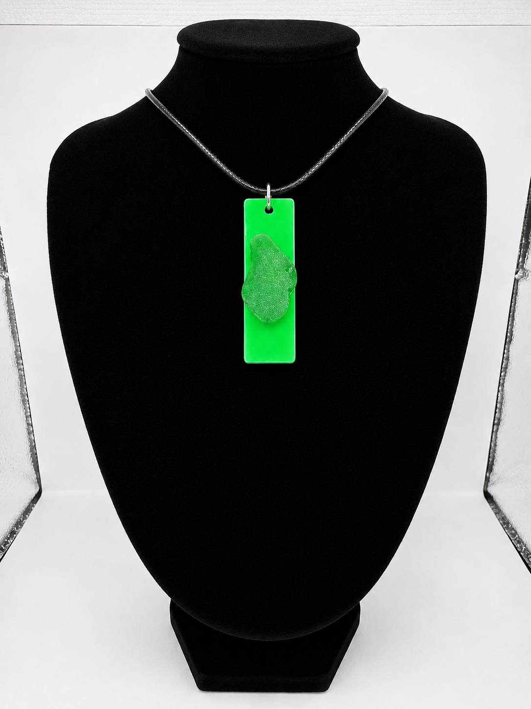 Sea glass pendant necklace on a green background with black waxed cord adjustable necklace