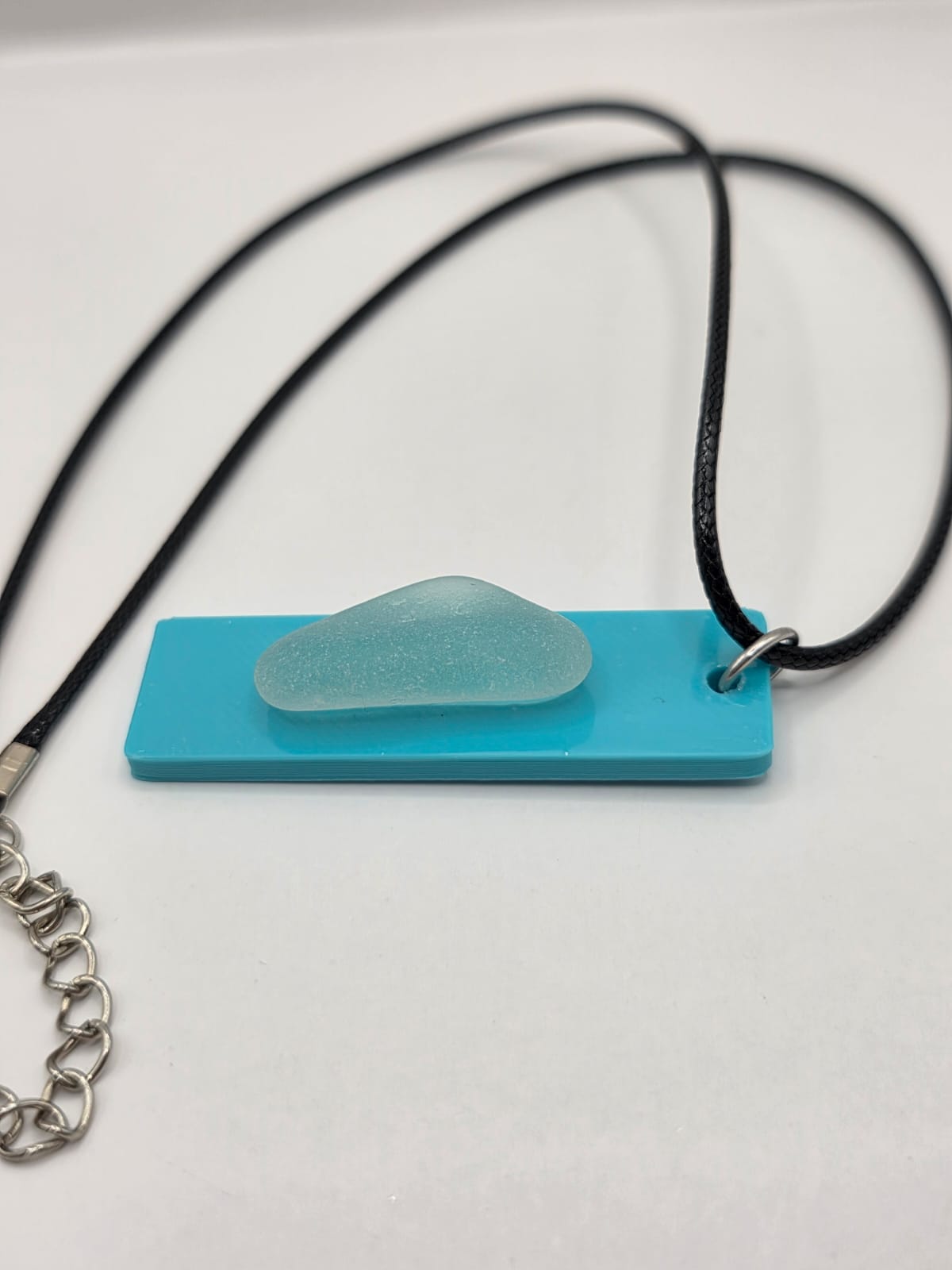 Sea glass pendant necklace on a light blue background with black waxed cord adjustable necklace