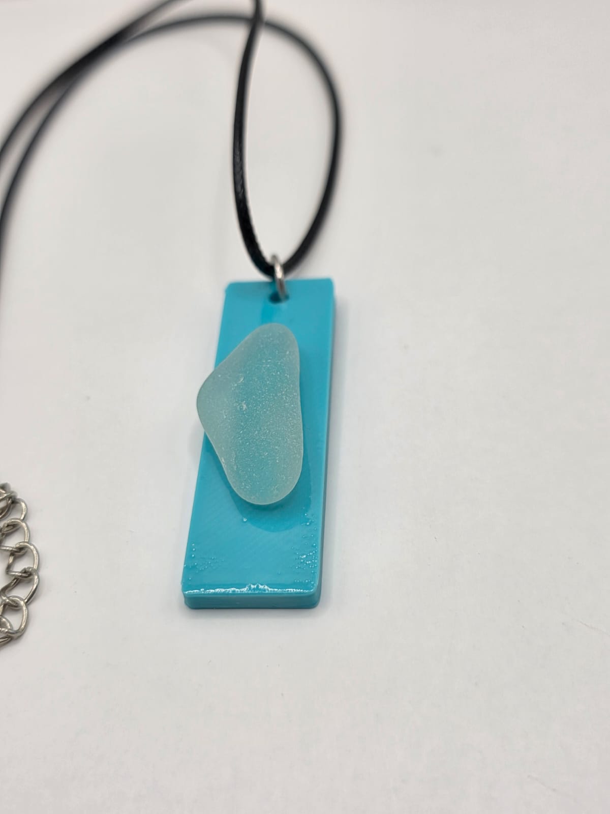 Sea glass pendant necklace on a light blue background with black waxed cord adjustable necklace