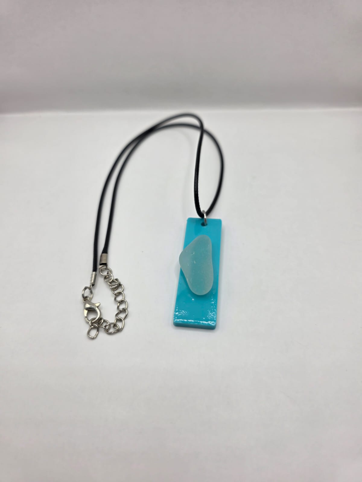 Sea glass pendant necklace on a light blue background with black waxed cord adjustable necklace