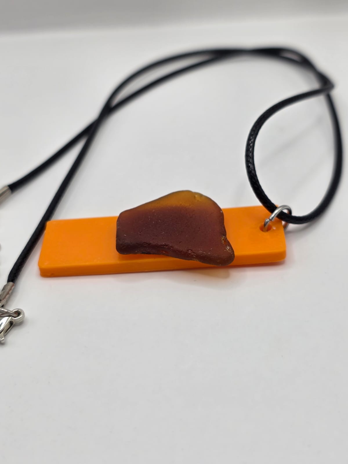 Sea glass pendant necklace on a orange background with black waxed cord adjustable necklace