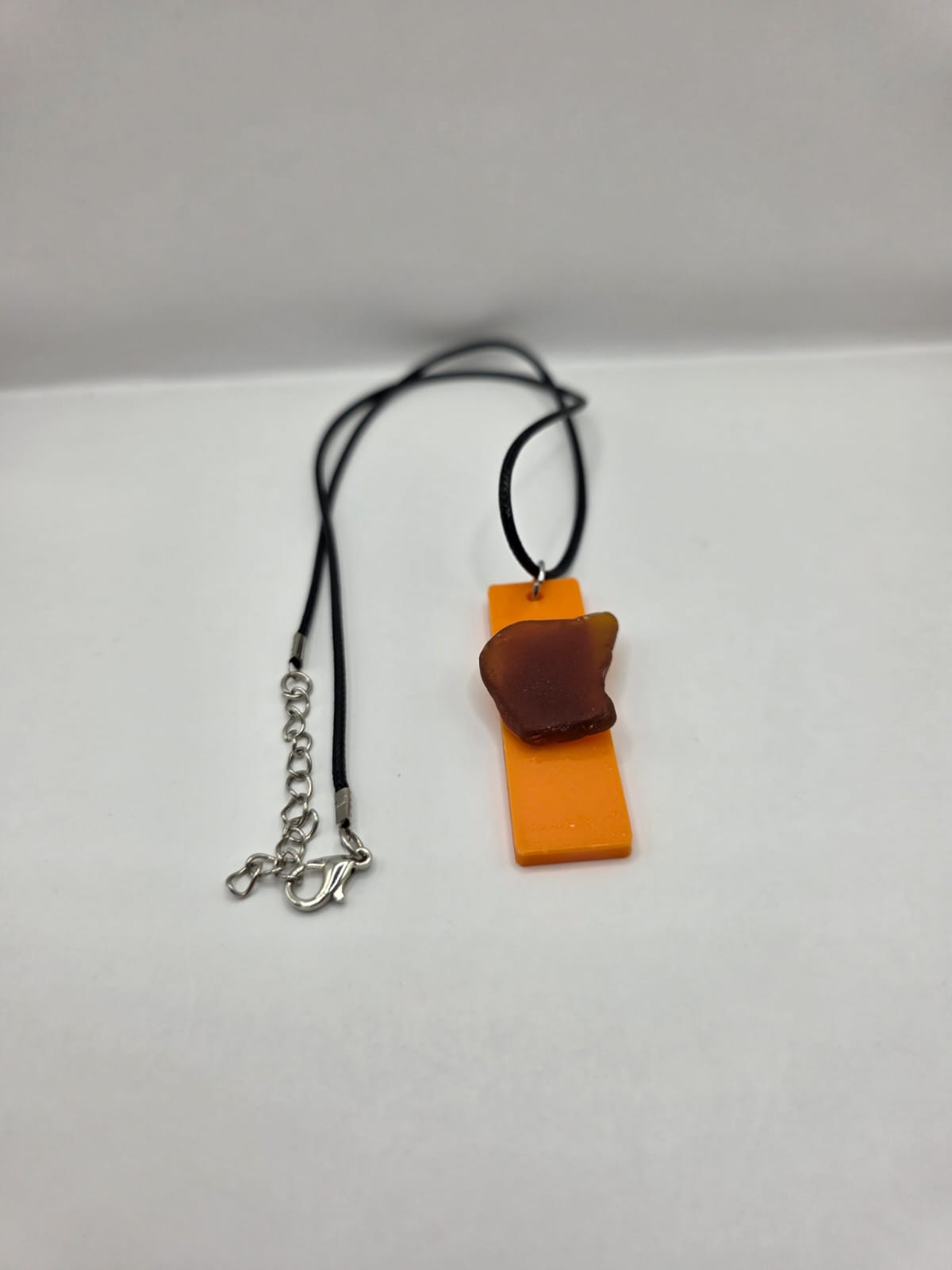 Sea glass pendant necklace on a orange background with black waxed cord adjustable necklace