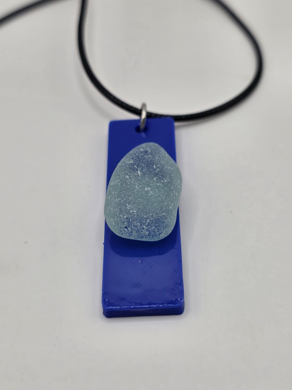 Sea glass pendant necklace on a blue background with black waxed cord adjustable necklace