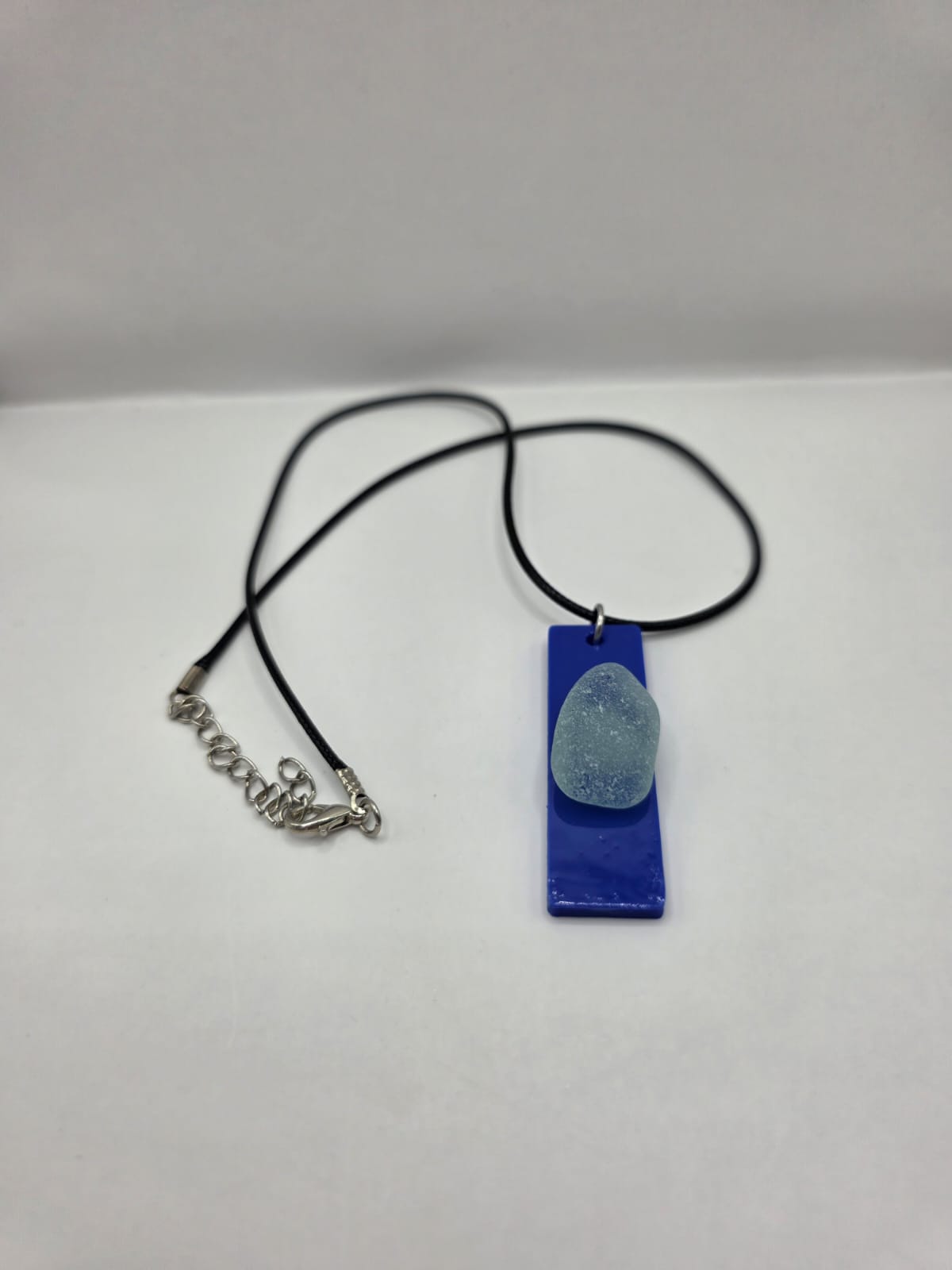 Sea glass pendant necklace on a blue background with black waxed cord adjustable necklace