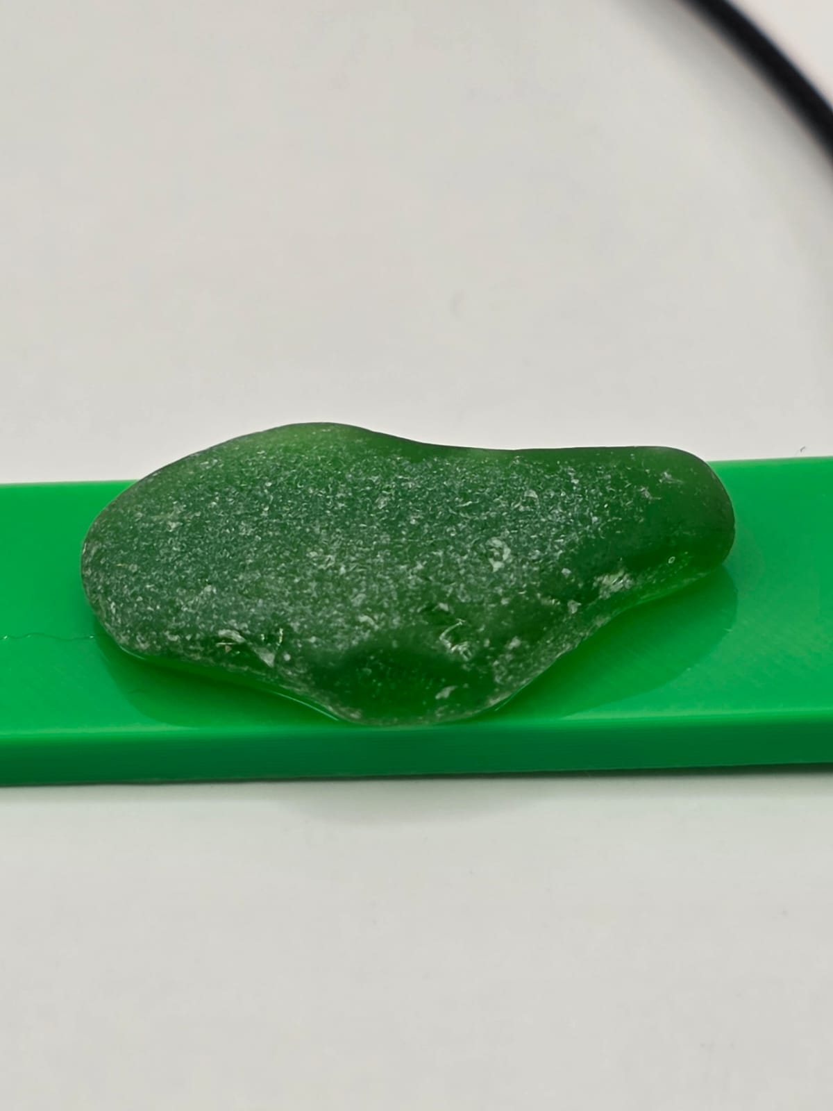 Sea glass pendant necklace on a green background with black waxed cord adjustable necklace