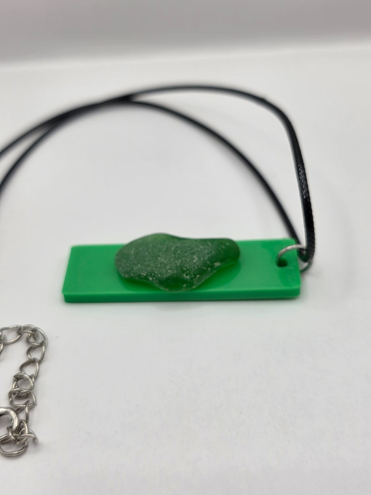 Sea glass pendant necklace on a green background with black waxed cord adjustable necklace