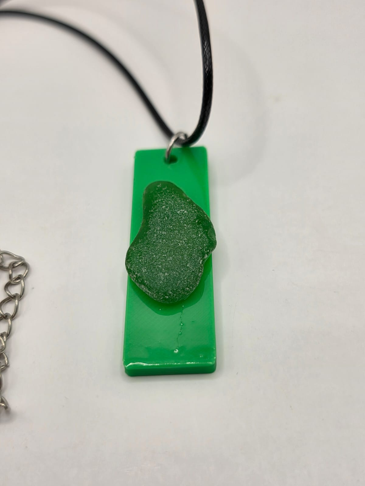 Sea glass pendant necklace on a green background with black waxed cord adjustable necklace