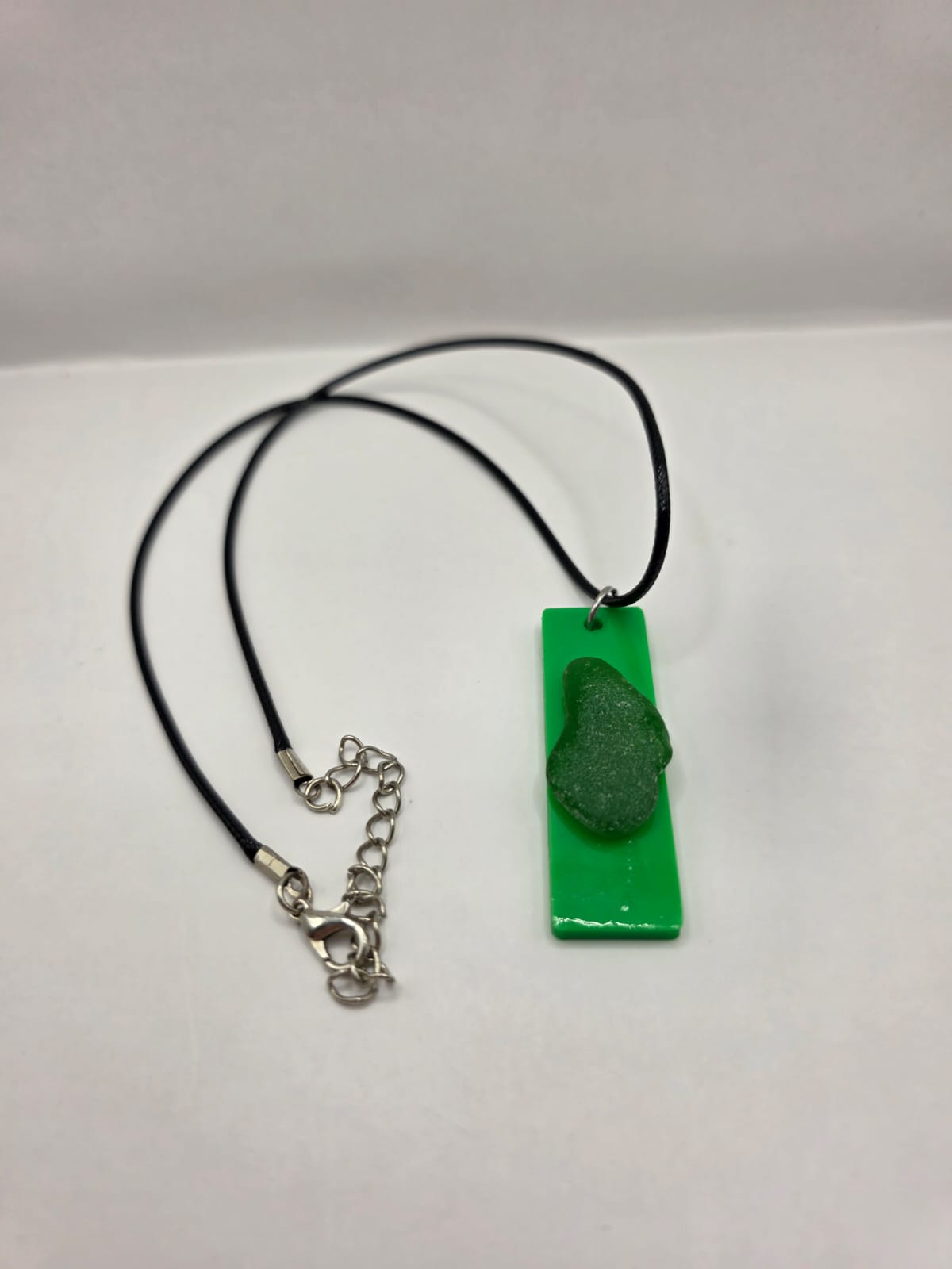 Sea glass pendant necklace on a green background with black waxed cord adjustable necklace