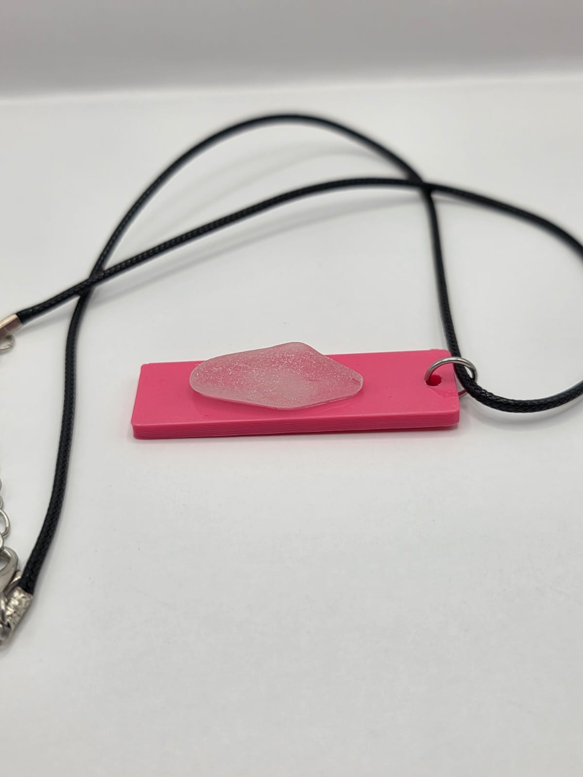 Sea glass pendant necklace on a pink background with black waxed cord adjustable necklace