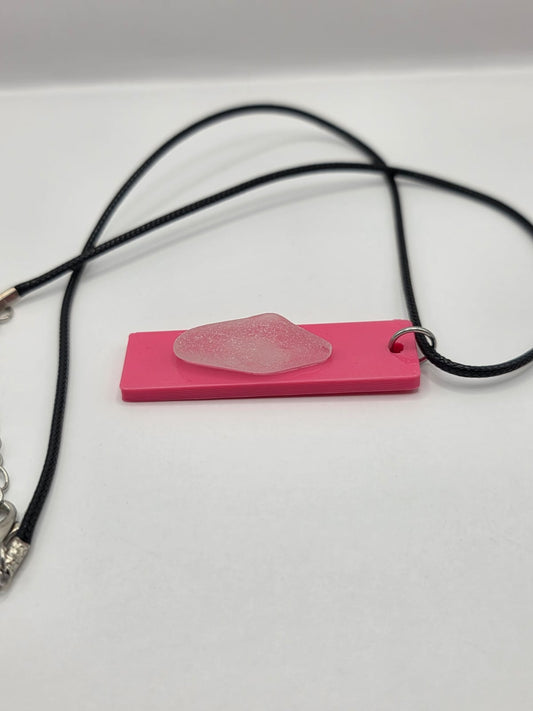 Sea glass pendant necklace on a pink background with black waxed cord adjustable necklace