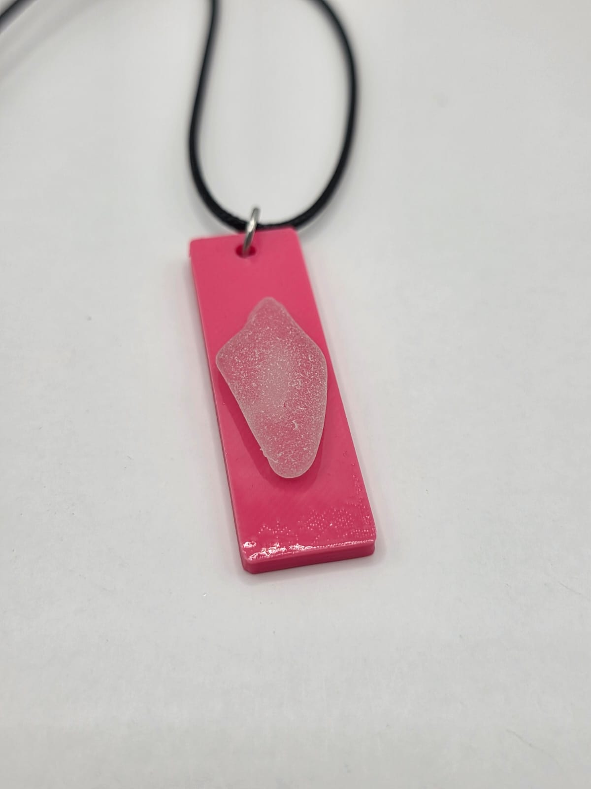 Sea glass pendant necklace on a pink background with black waxed cord adjustable necklace