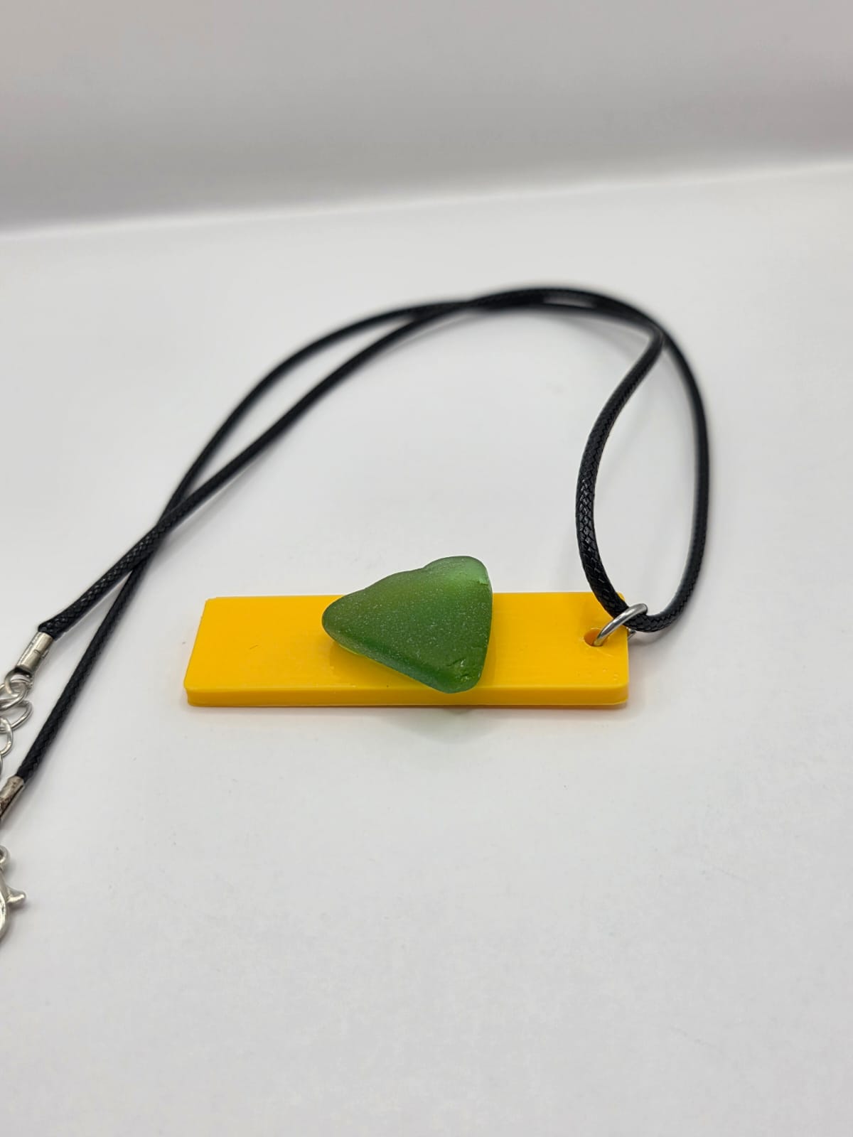 Sea glass pendant necklace on a yellow background with black waxed cord adjustable necklace