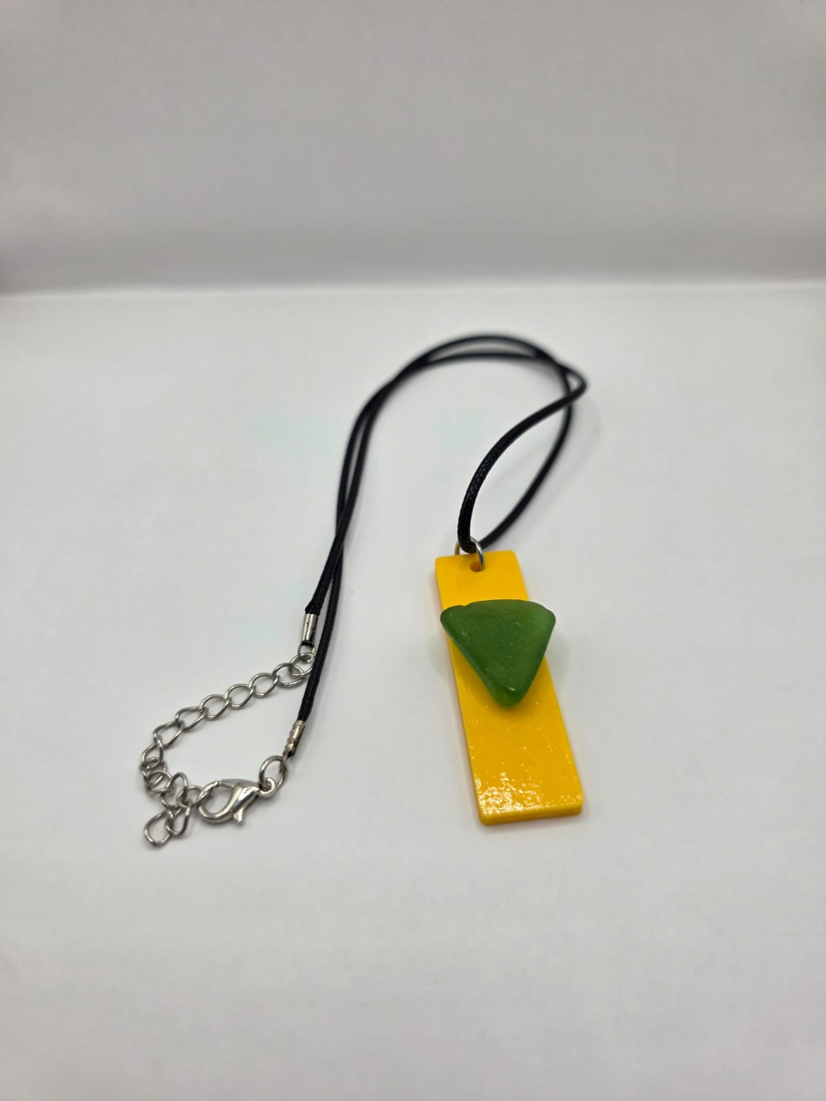 Sea glass pendant necklace on a yellow background with black waxed cord adjustable necklace