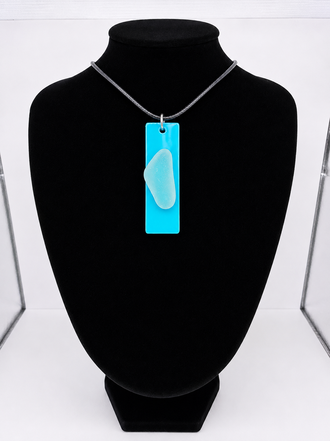Sea glass pendant necklace on a light blue background with black waxed cord adjustable necklace