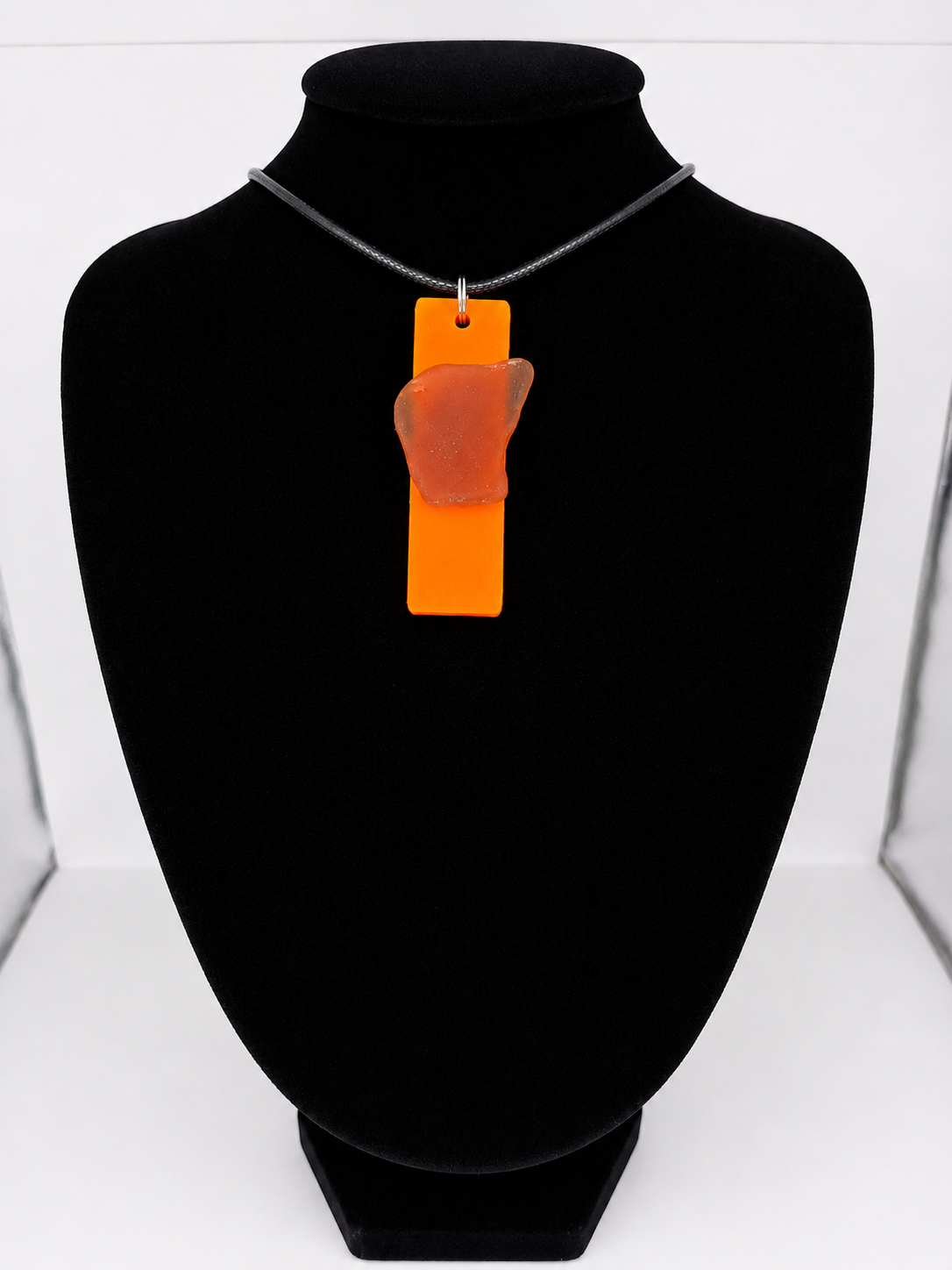 Sea glass pendant necklace on a orange background with black waxed cord adjustable necklace