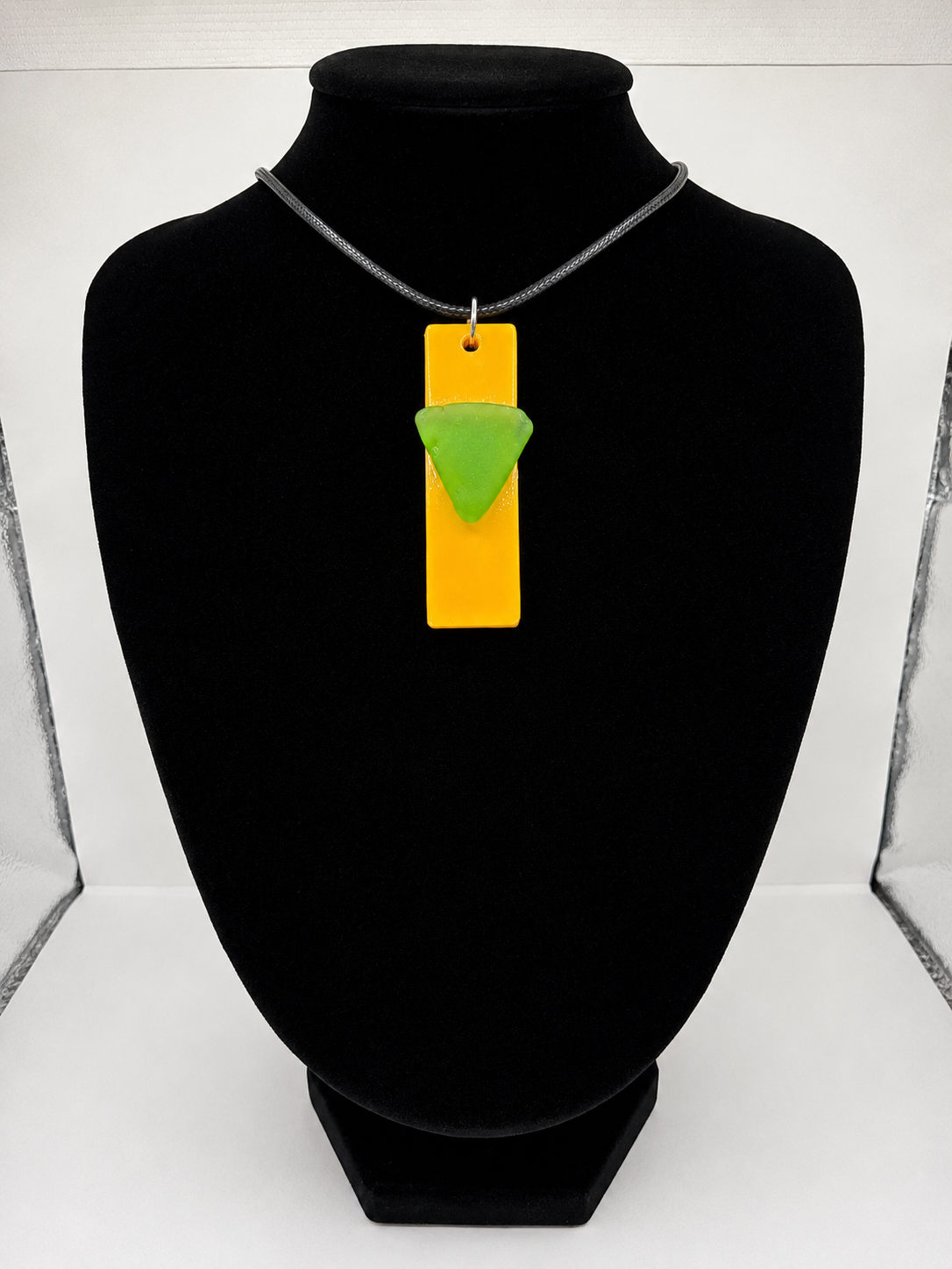 Sea glass pendant necklace on a yellow background with black waxed cord adjustable necklace
